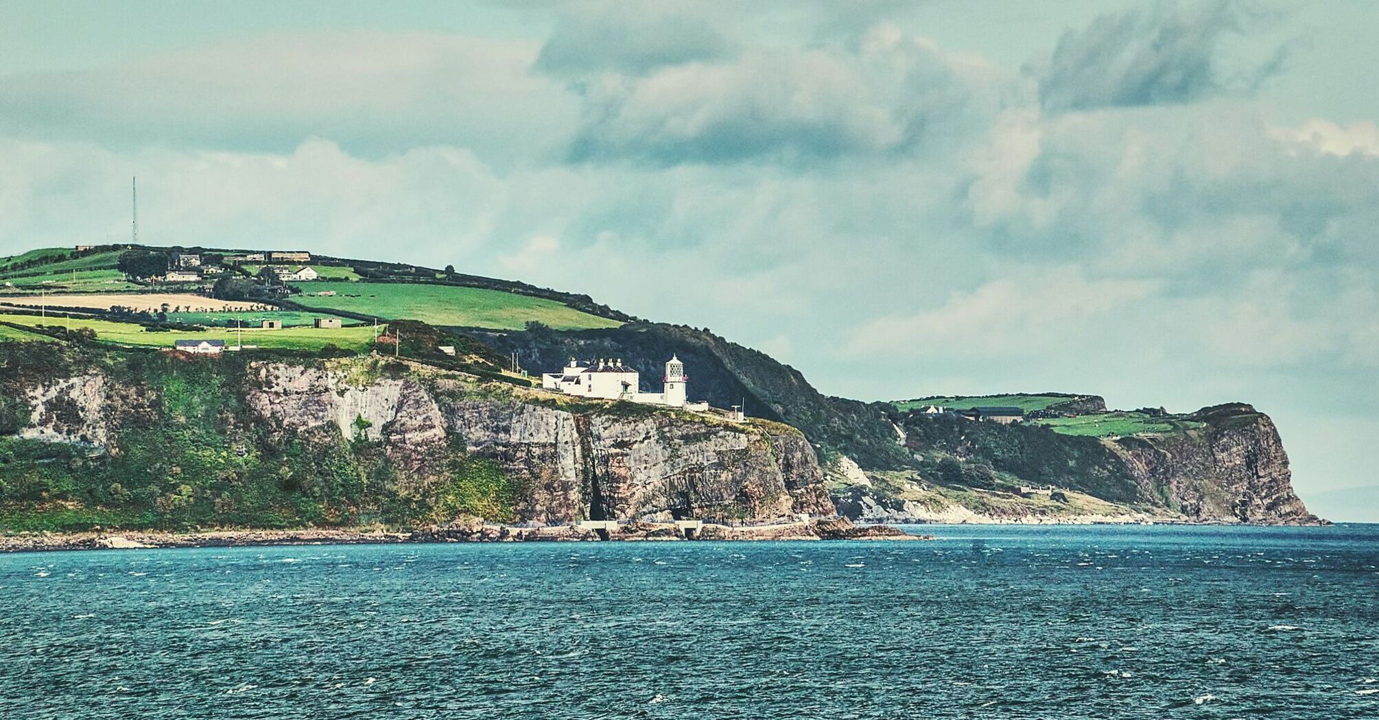 Coastal cliffs with a lighthouse overlooking the North Atlantic Ocean under a partly cloudy sky