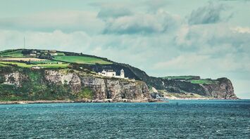 Coastal cliffs with a lighthouse overlooking the North Atlantic Ocean under a partly cloudy sky