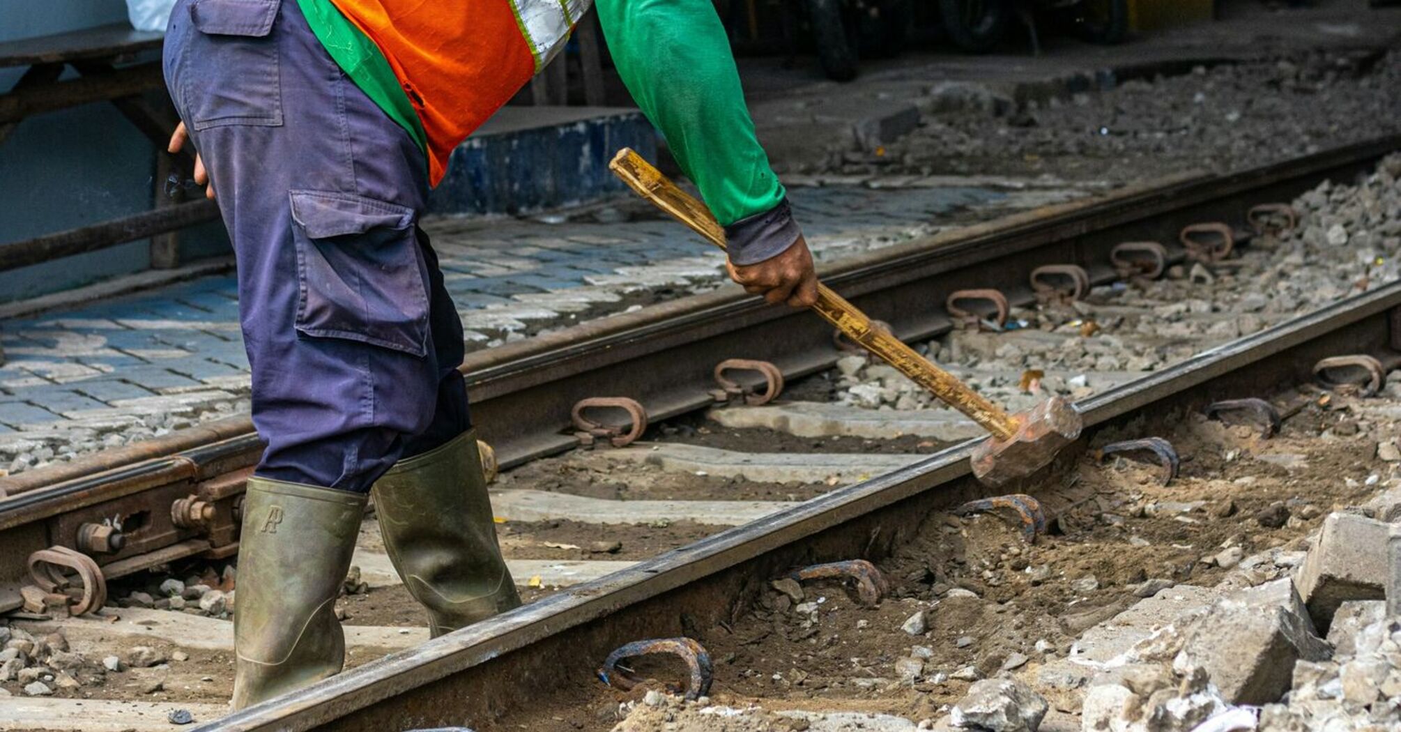 A railway worker in protective gear using a hammer to maintain train tracks