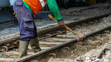 A railway worker in protective gear using a hammer to maintain train tracks