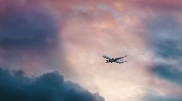 A commercial airplane flies through a dramatic sky with dark and colorful clouds