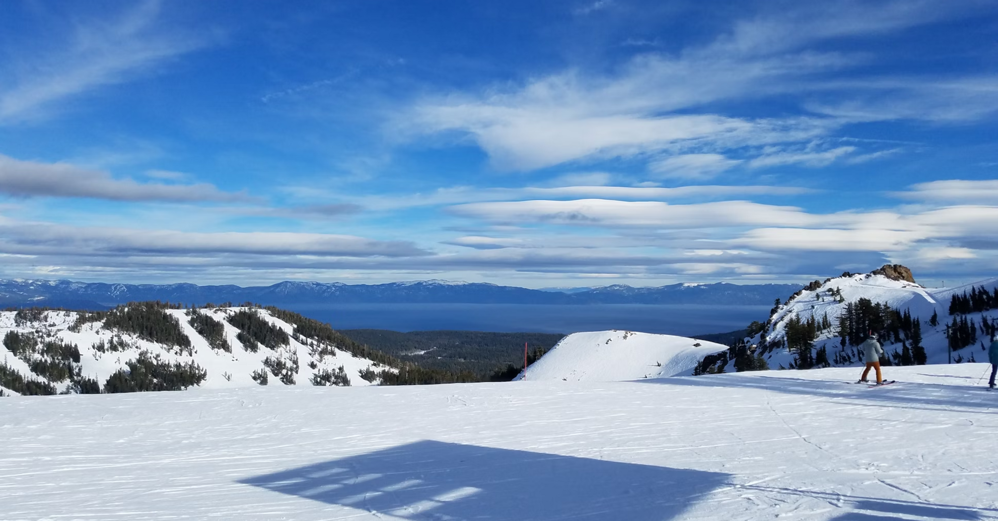 Snowy mountain landscape with skiers and a scenic view of distant peaks under a bright blue sky