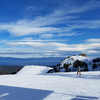 Snowy mountain landscape with skiers and a scenic view of distant peaks under a bright blue sky