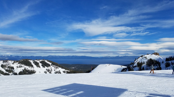 Snowy mountain landscape with skiers and a scenic view of distant peaks under a bright blue sky