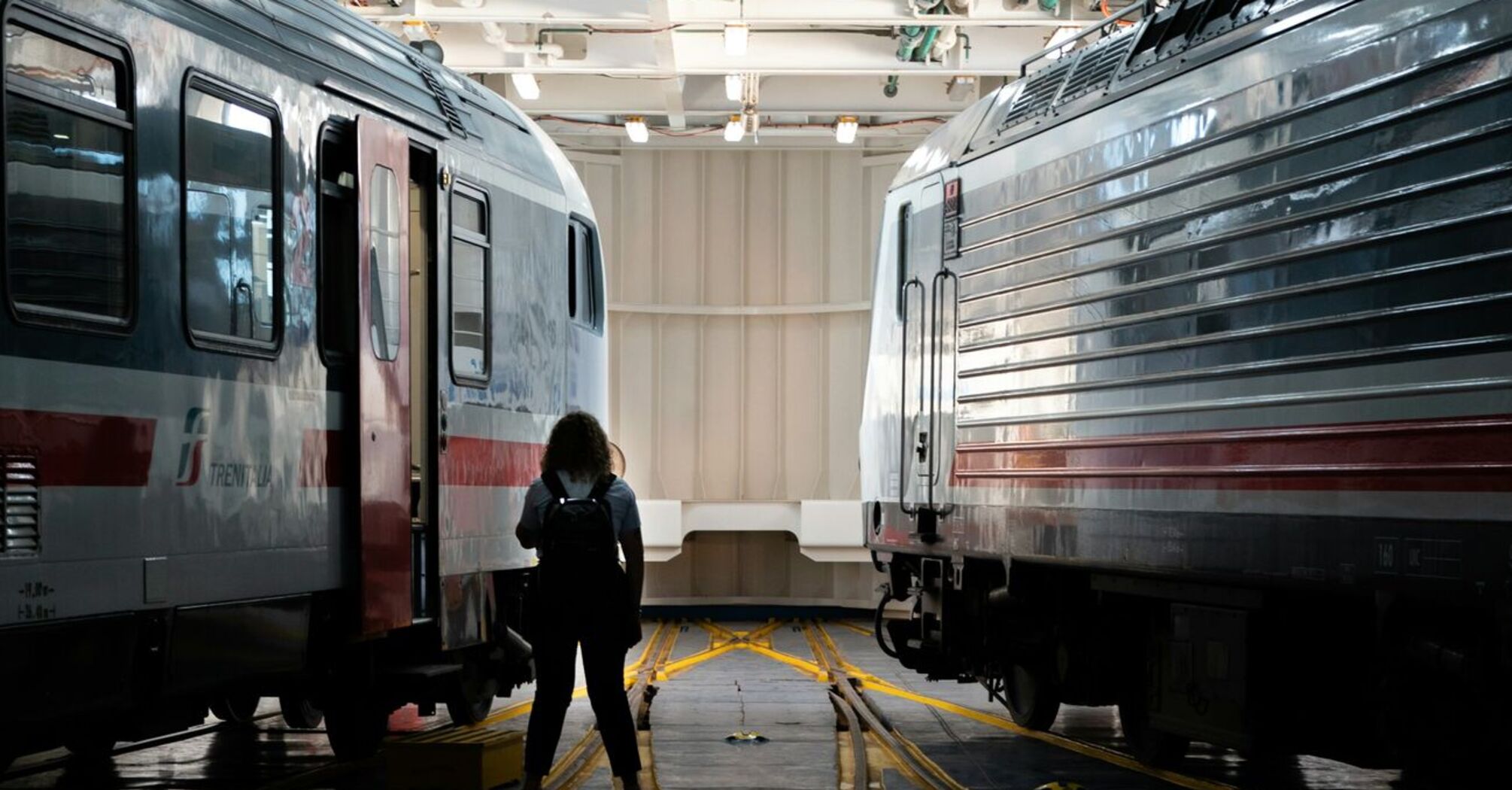 A Trenitalia Intercity train inside a ferry, with a person walking along the tracks