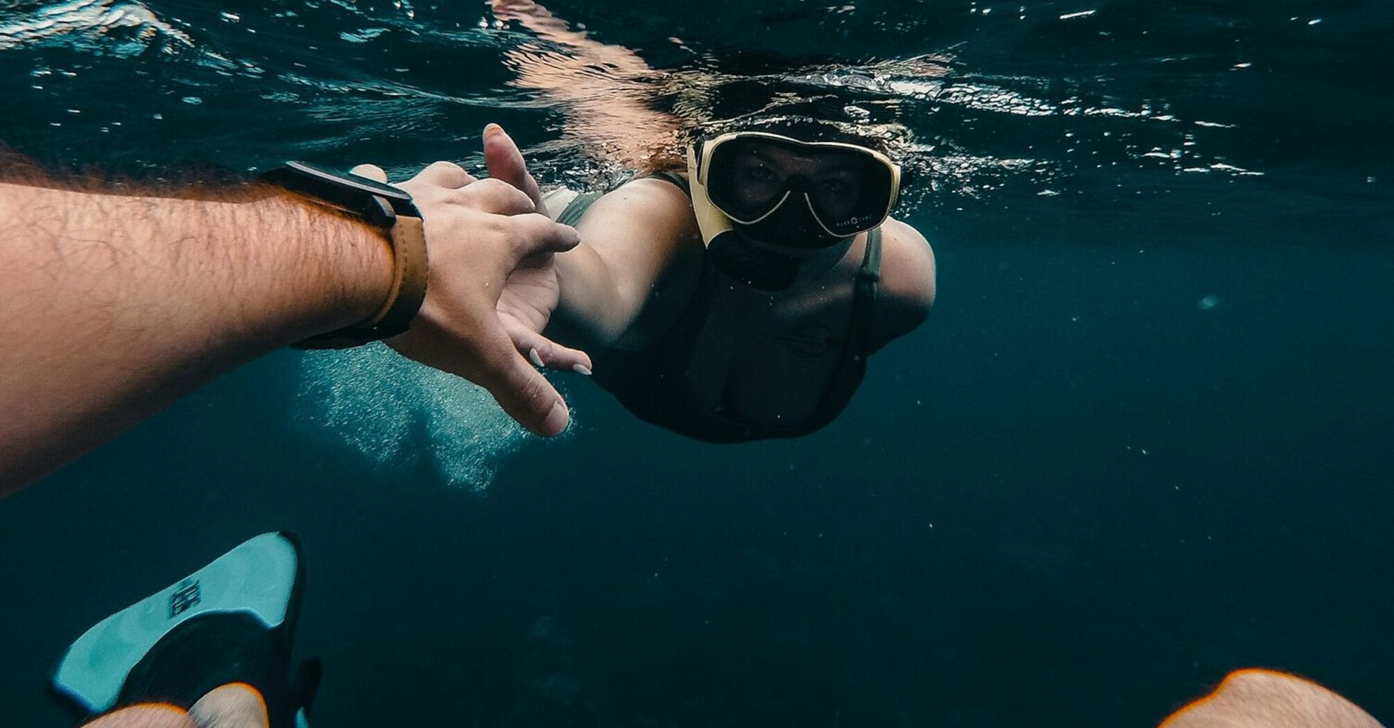 A snorkeler underwater reaching for a companion's hand while exploring the ocean