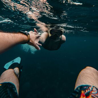 A snorkeler underwater reaching for a companion's hand while exploring the ocean