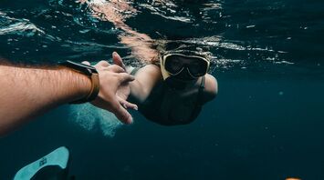 A snorkeler underwater reaching for a companion's hand while exploring the ocean