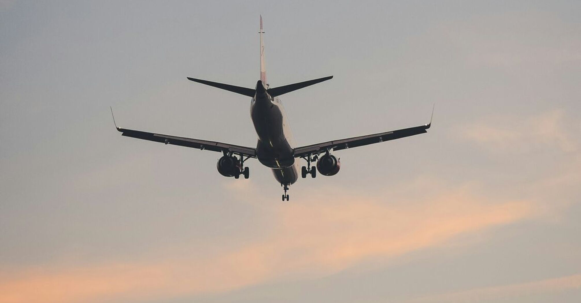 A commercial airplane approaching for landing against a pastel-colored sky at dusk