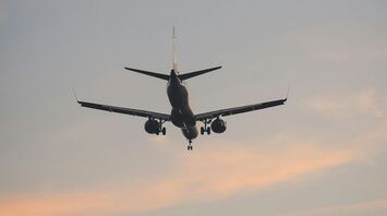 A commercial airplane approaching for landing against a pastel-colored sky at dusk