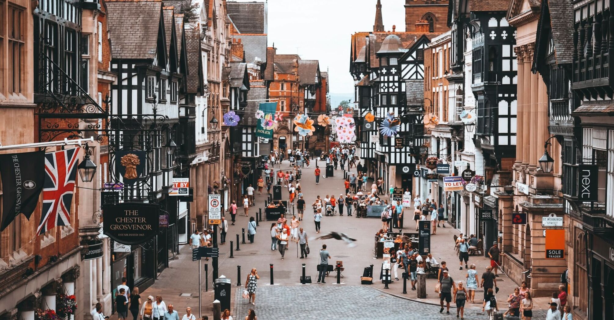 Bustling pedestrian street in Chester with historic black-and-white timber buildings, shops, and outdoor cafes