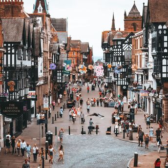 Bustling pedestrian street in Chester with historic black-and-white timber buildings, shops, and outdoor cafes