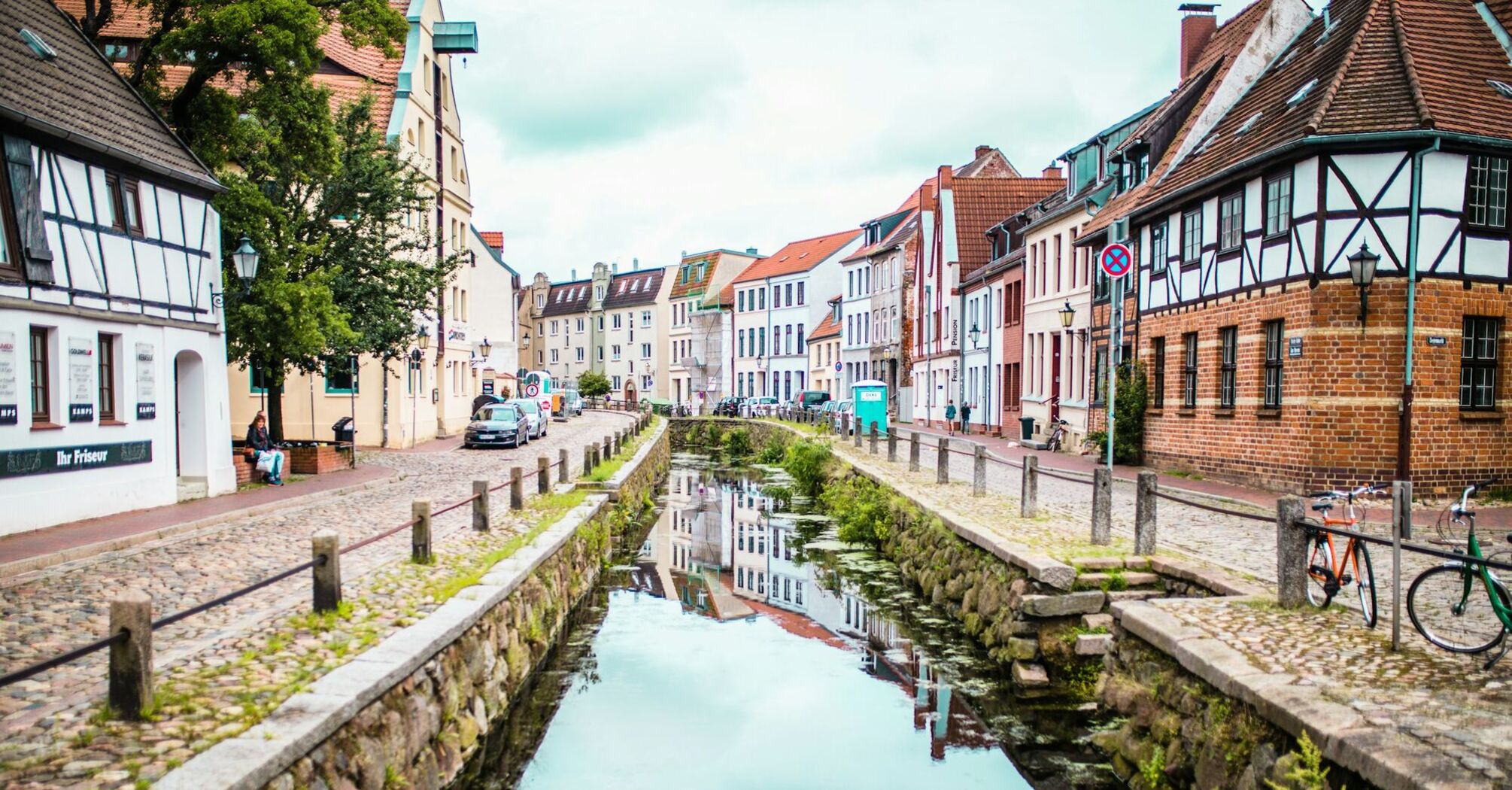 A historic red-brick building in Wismar, Germany, reflected in a calm canal on a foggy day