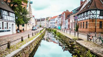 A historic red-brick building in Wismar, Germany, reflected in a calm canal on a foggy day