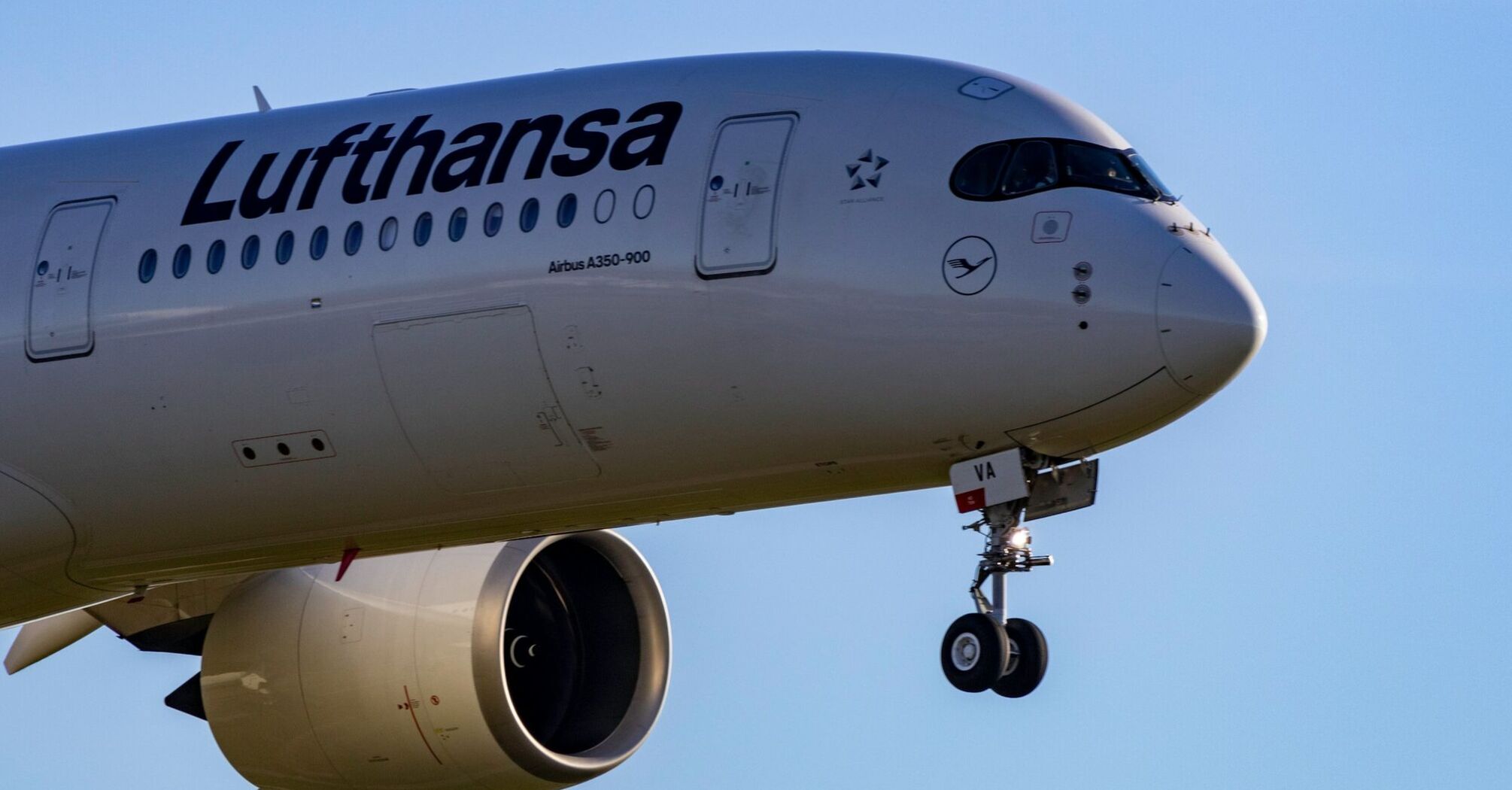 Lufthansa Airbus A350-900 landing with extended landing gear against a clear blue sky