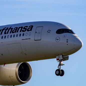 Lufthansa Airbus A350-900 landing with extended landing gear against a clear blue sky