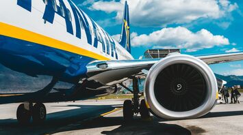 A Ryanair aircraft parked at the airport with a clear blue sky and passengers boarding in the background