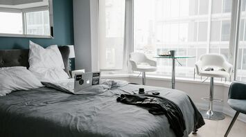 A modern hotel room with a large bed, a laptop, and a small seating area by the window overlooking a cityscape