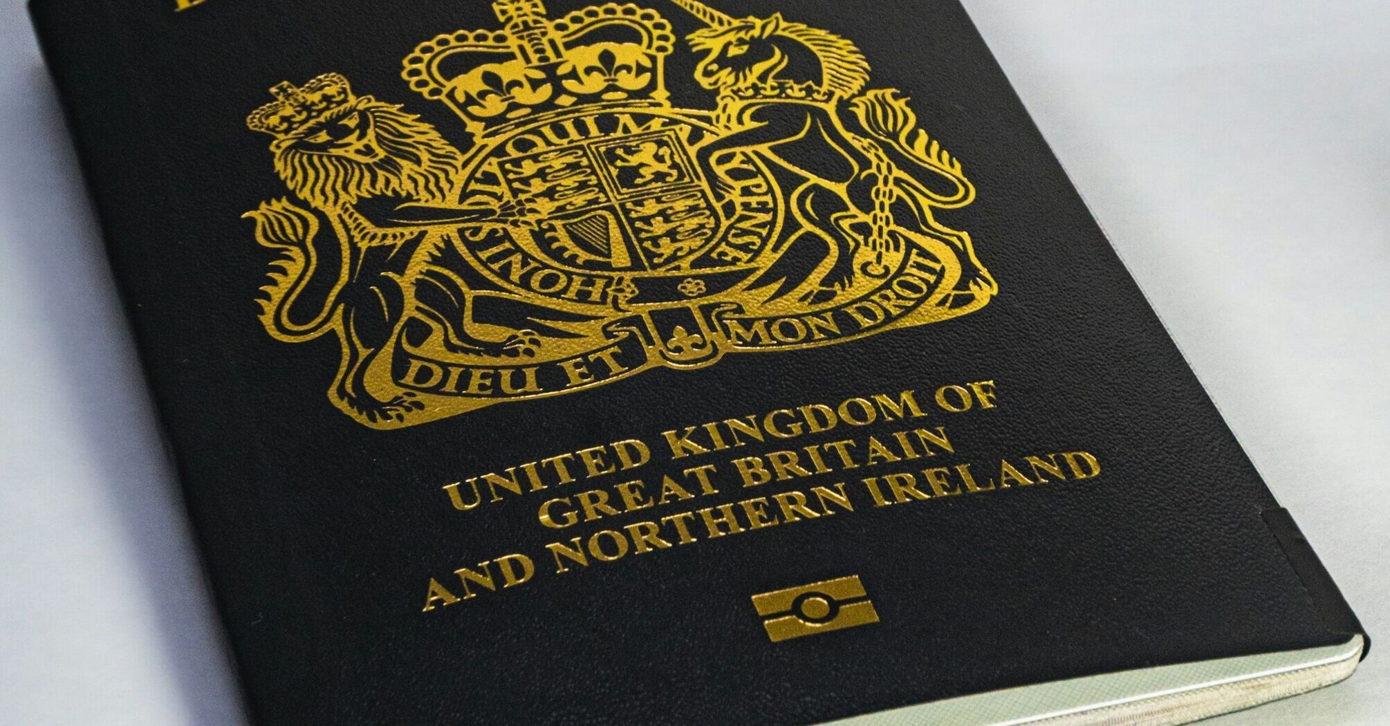 A close-up of a black British passport with a gold emblem on a white surface