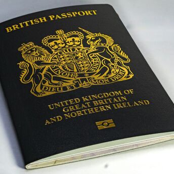 A close-up of a black British passport with a gold emblem on a white surface