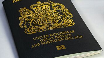A close-up of a black British passport with a gold emblem on a white surface
