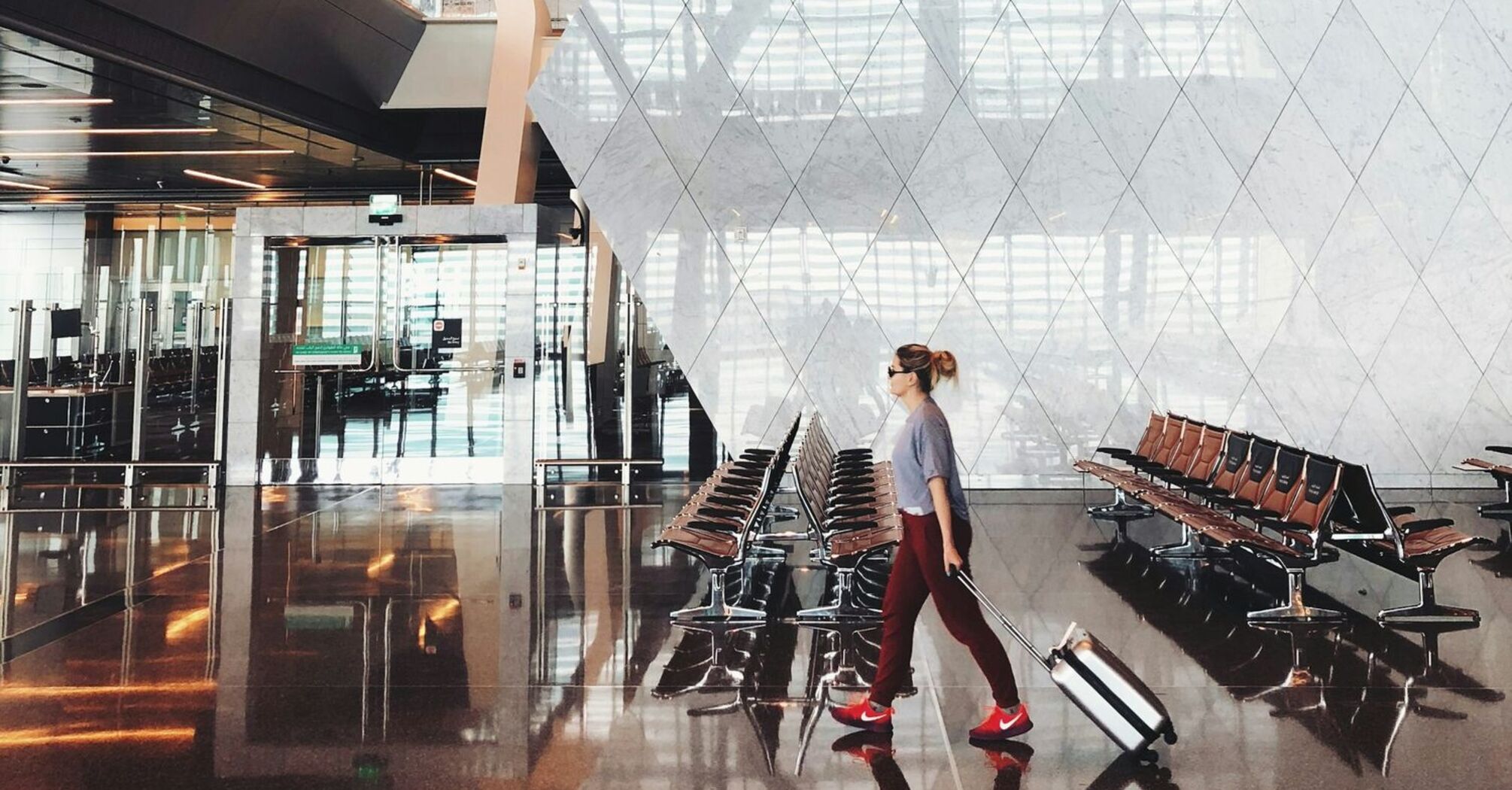 A traveler with a suitcase walks through Hamad International Airport's modern terminal, featuring sleek architecture and spacious seating areas