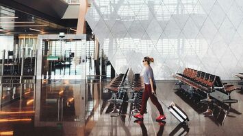 A traveler with a suitcase walks through Hamad International Airport's modern terminal, featuring sleek architecture and spacious seating areas