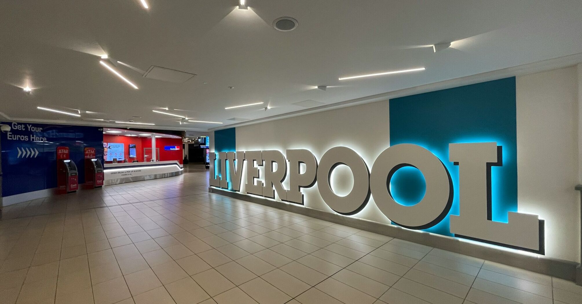 Interior of Liverpool John Lennon Airport with illuminated Liverpool sign and currency exchange area