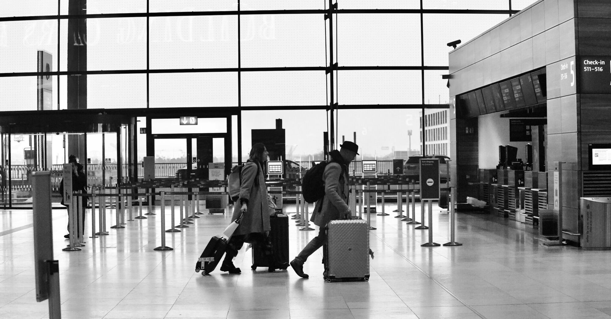 Travelers pulling luggage through a nearly empty airport check-in area