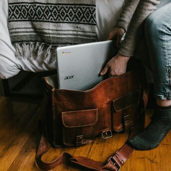 Person placing an Acer Chromebook into a leather travel bag beside a bed