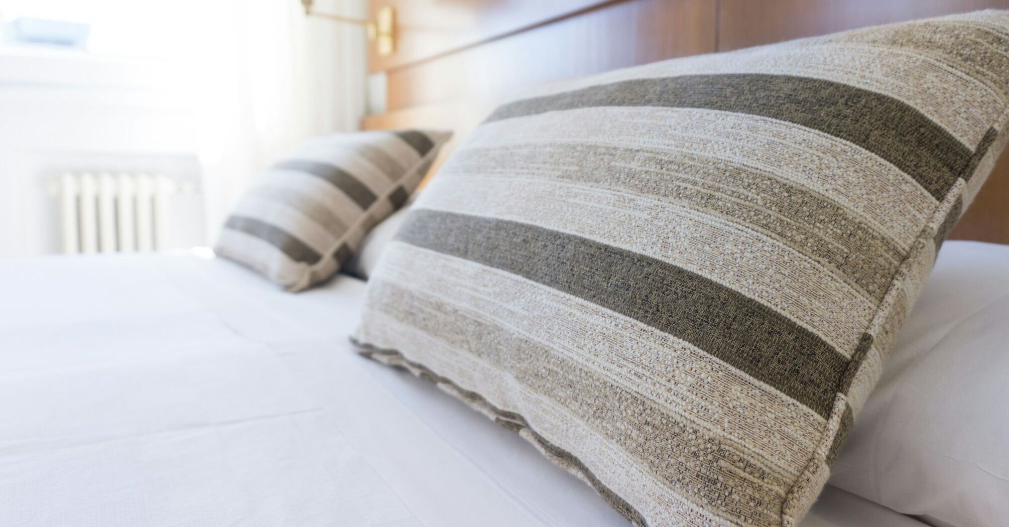 Striped pillows on a neatly made hotel bed in a bright, modern room