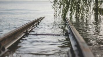 Flooded railway tracks disappearing into a body of water with overhanging tree branches