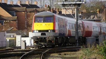A First Class train operated by Transport for Wales approaching a station through a residential area