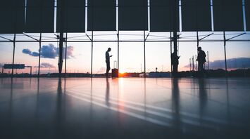 Silhouettes of travellers waiting at an airport terminal during sunset