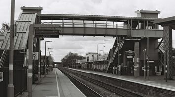 A quiet British railway station with footbridge and empty platforms on a cloudy day