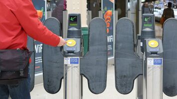 A passenger taps their card at a train station ticket barrier using contactless payment