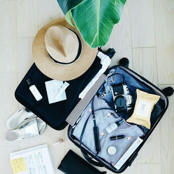 Open suitcase with travel essentials, camera, summer clothes, and accessories laid out on a wooden floor