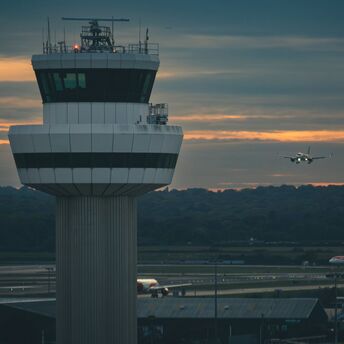 Air traffic control tower at Gatwick Airport with a plane landing at sunset