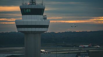 Air traffic control tower at Gatwick Airport with a plane landing at sunset