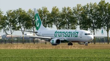 A Transavia aircraft on the runway, surrounded by greenery, preparing for departure