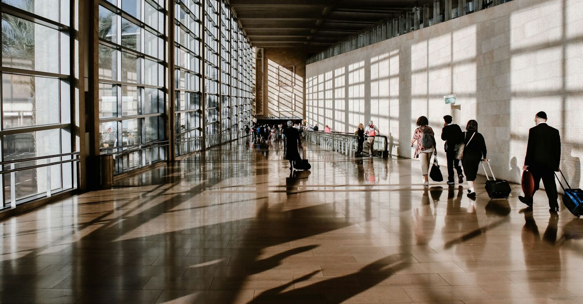 Travelers walking through a modern airport terminal with large glass windows