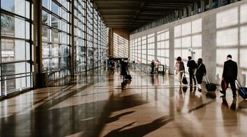 Travelers walking through a modern airport terminal with large glass windows