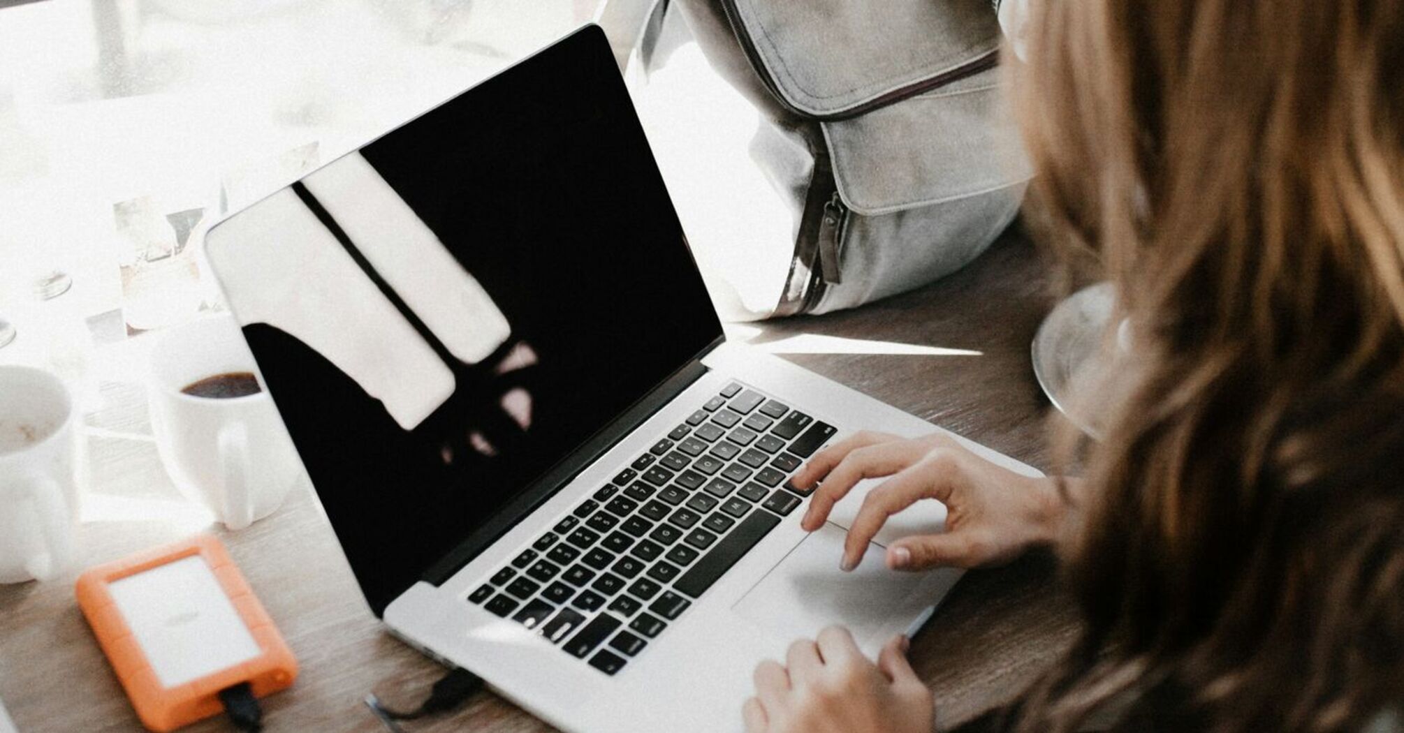 A woman with an open laptop at a café with a backpack beside her