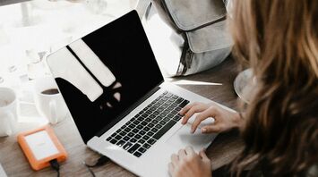 A woman with an open laptop at a café with a backpack beside her