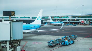 Two KLM airplanes parked at the airport gate with baggage handling equipment on the tarmac