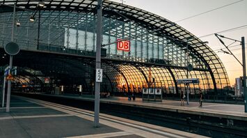 A modern glass-structured railway station with a "DB" sign and a sunset in the background, indicating Berlin Hauptbahnhof