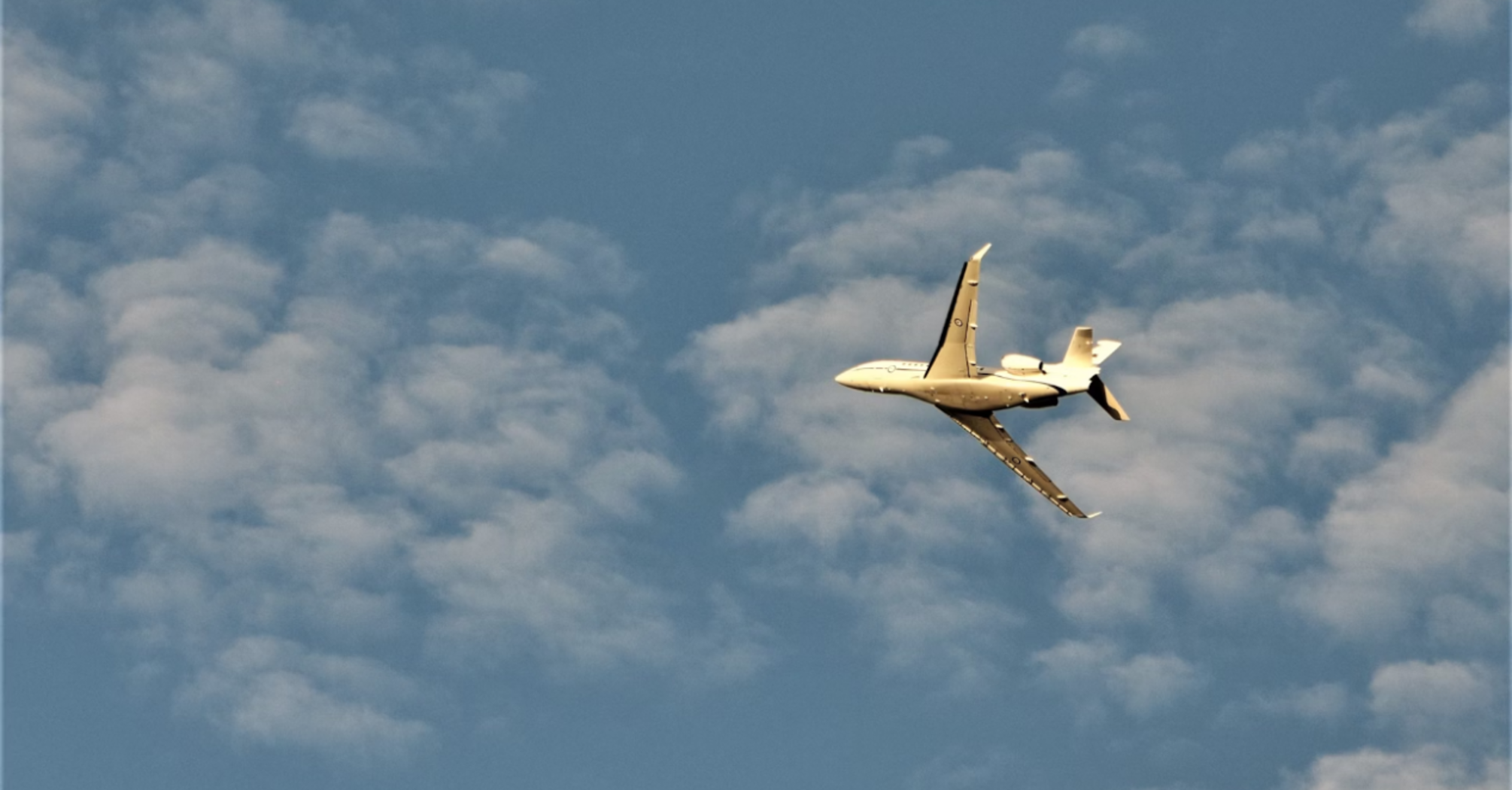 Private jet flying through a blue sky with scattered clouds