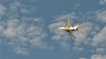 Private jet flying through a blue sky with scattered clouds