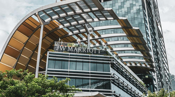 Modern glass high-rise JW Marriott hotel with a sleek architectural design under a blue sky with clouds
