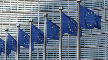 Rows of European Union flags waving in front of a modern glass building